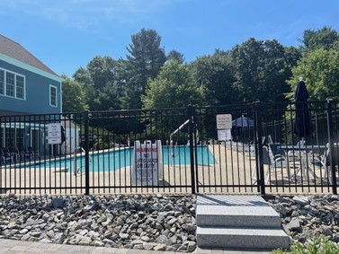 An empty swimming pool with a No Lifeguard on Duty sign at the gate.