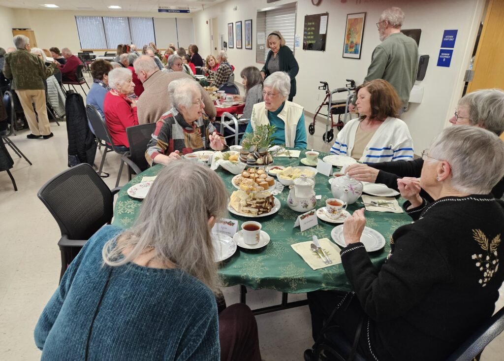 On one table, there is a china teapot, china teacups, and a three-tiered tray filled with baked goods.