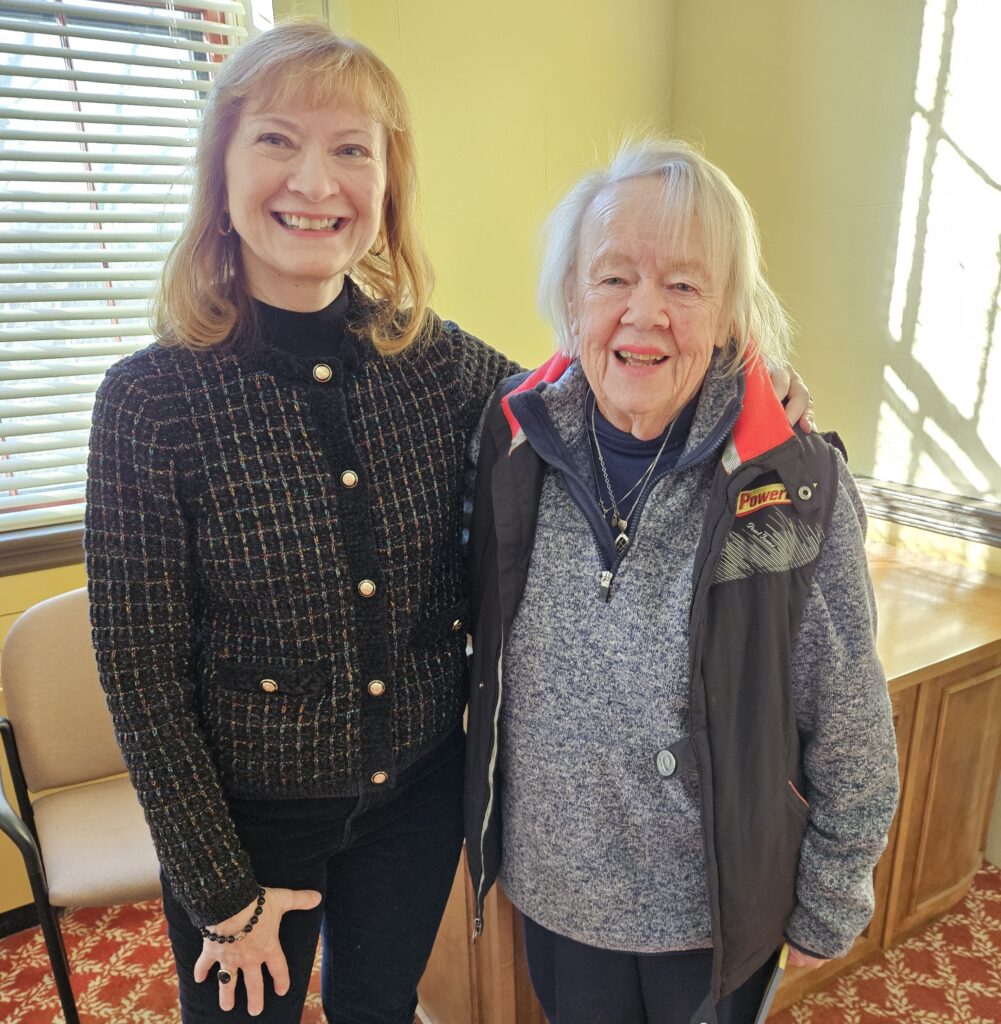 Two women, one with blond hair and one with gray hair, stand next to each other in Room 204.