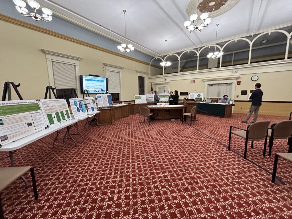 Room 204 with posters and tables lined up on the left and chairs on the right. A few people are milling around, waiting for the open house to start.