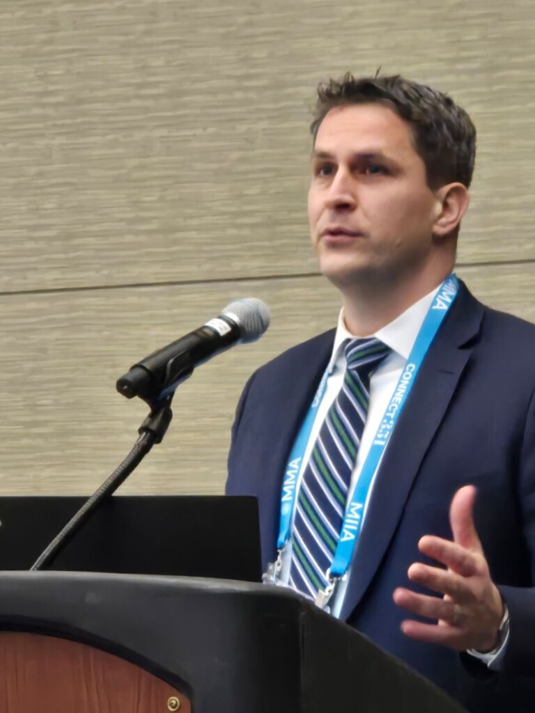 A man wearing a suit and tie speaks into a mic at a podium.