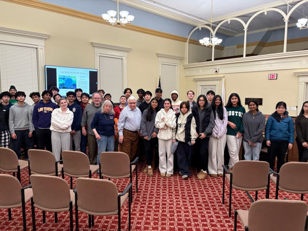 A group photo with three older people in the front, surrounded by a horde of high school students.