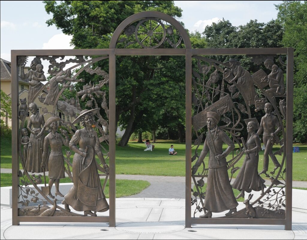 A beautifully carved bronze gate to nowhere in the middle of a park. Each side of the gate is covered with a spiral of femal figures walking towards the center.