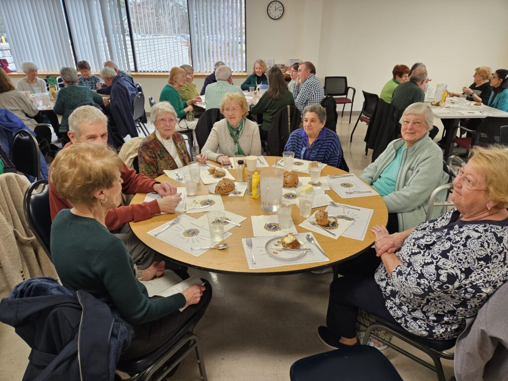 A table full of people eating and chatting. There are several other full tables in the background.