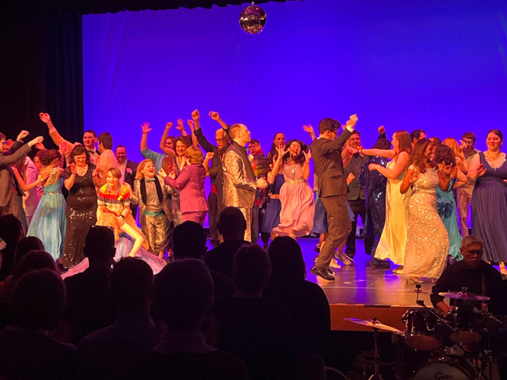 Colorful dancers on stage with silhouetted audience in foreground.