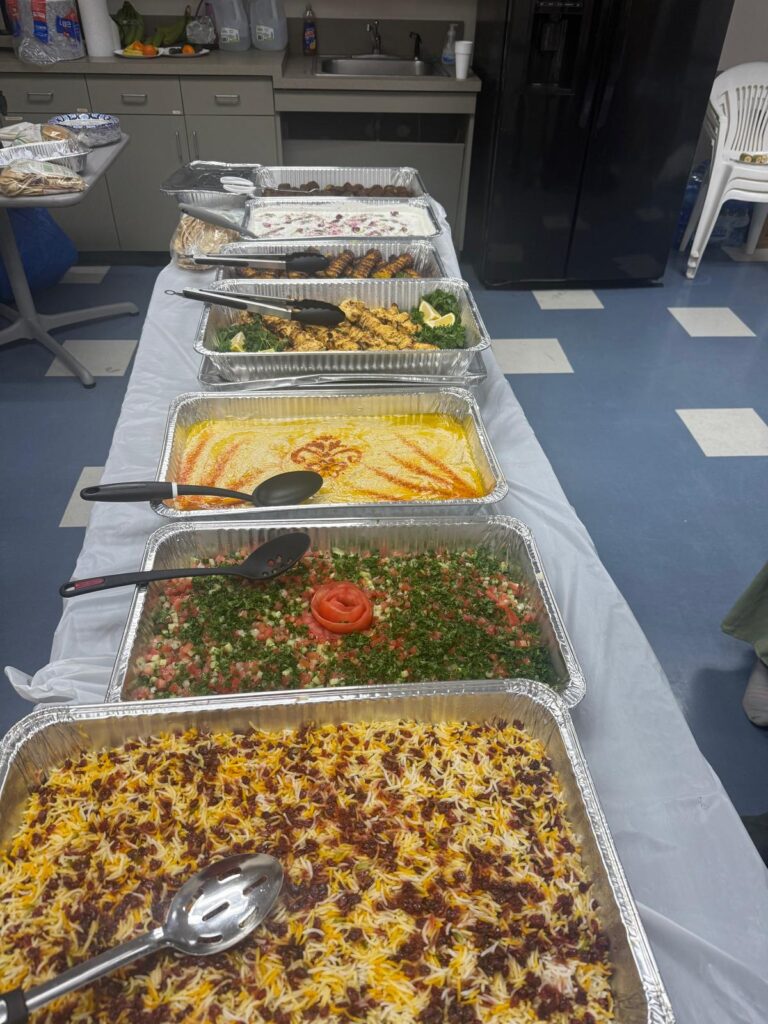 A table with a row of catering trays full of delicious-looking food including rice and beans and tabouli salad.