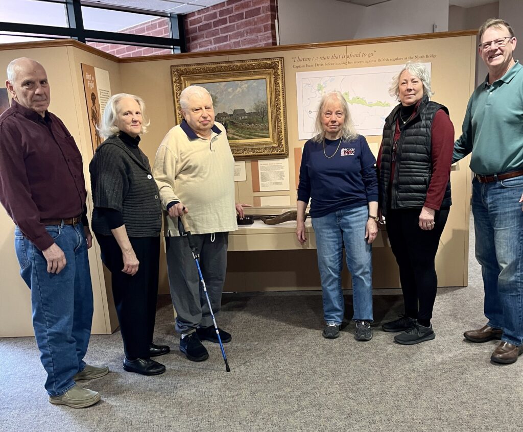 Several people pose in front of the Colonial history exhibit at the Acton Memorial Library.