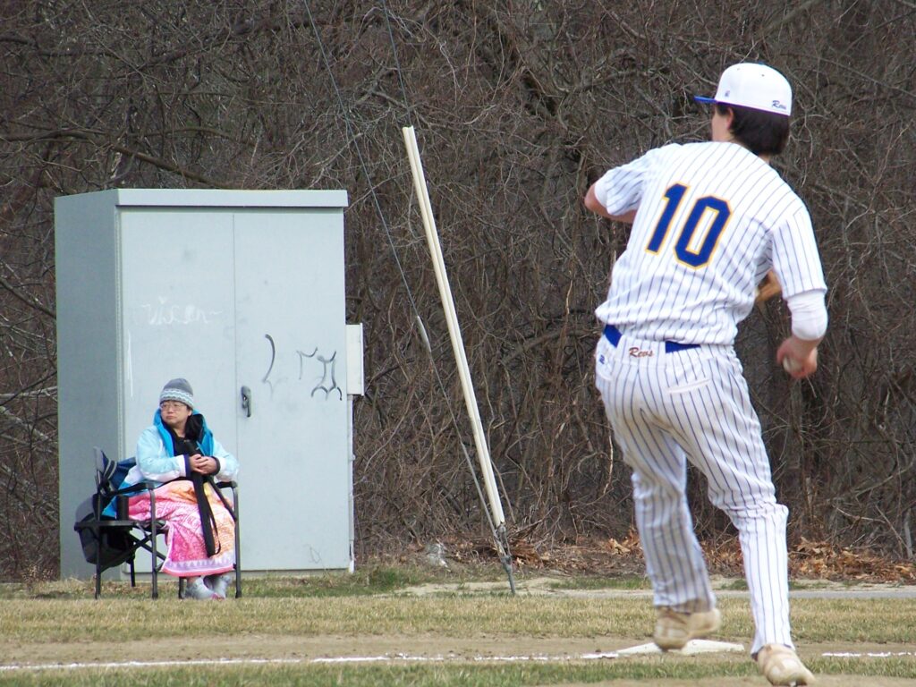 A Revs player gets ready to throw the ball that is in his hand. In the background, a woman watches the game.