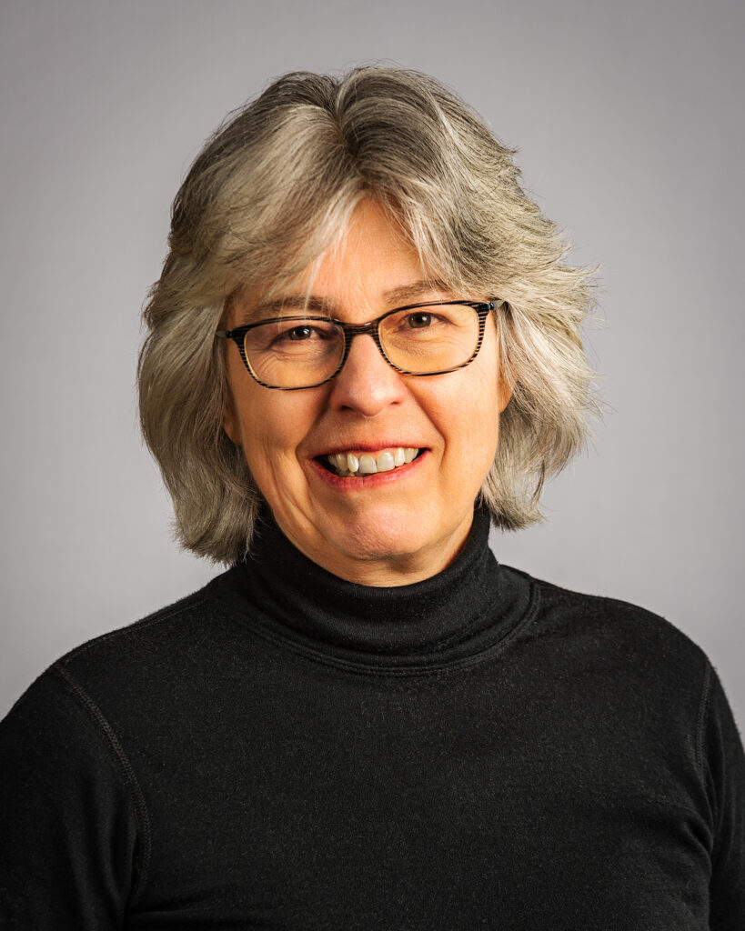 A smiling woman with salt and pepper hair and glasses.