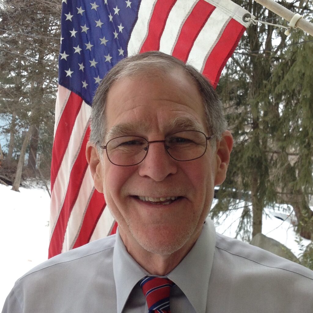 A smiling man with snow and an American flag in the background.