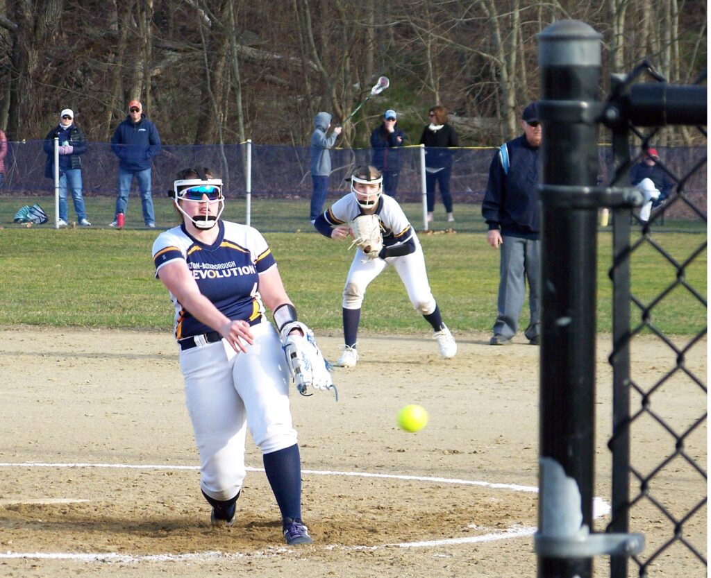 A Revs player pitches a ball towards a batter. The first basewoman is ready in the background.