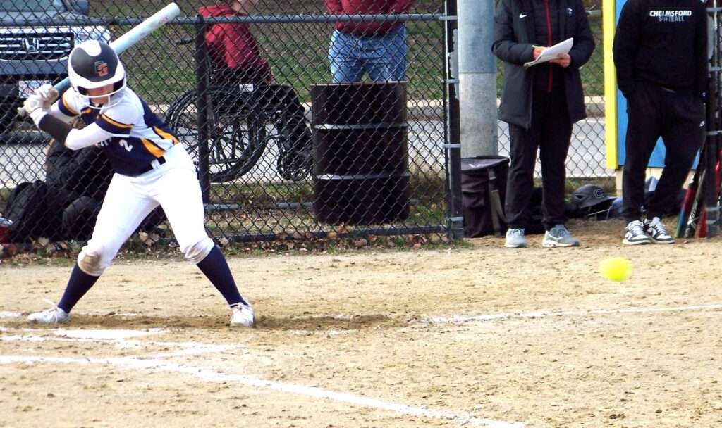 A softball player in a Revs uniform starts swinging at an incoming ball.