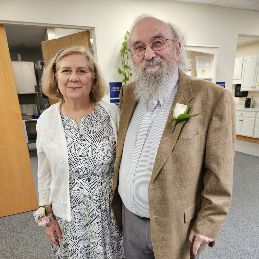 A couple, newly-adorned in boutonneire and corsage, and all dressed up, stand at the entrance of the prom.