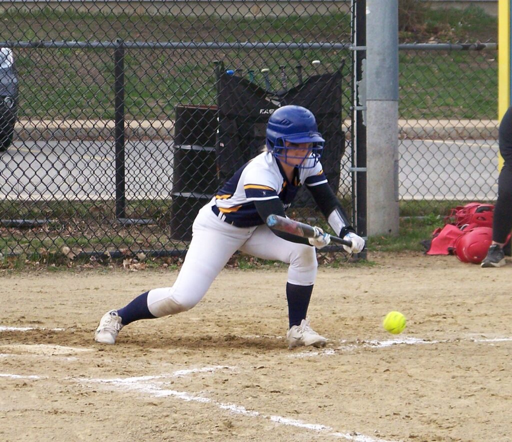 A Revs player bunts a ball. The ball is still in the air, but only about 3 inches off the ground.