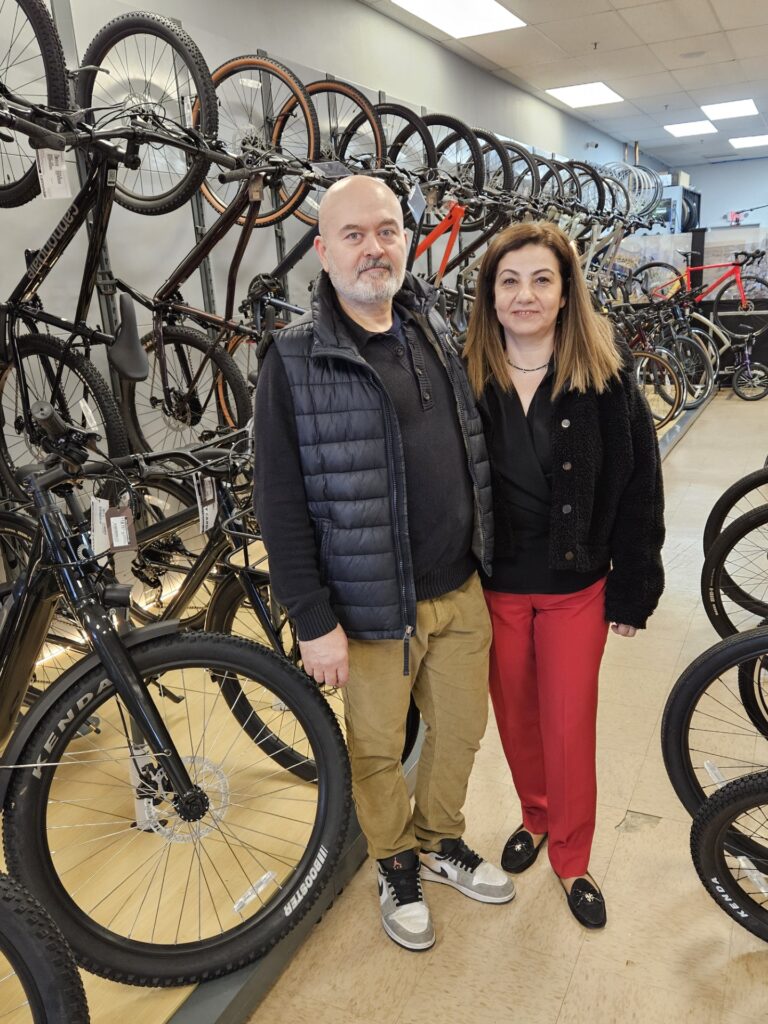 A couple pose in front of a wall of bikes.