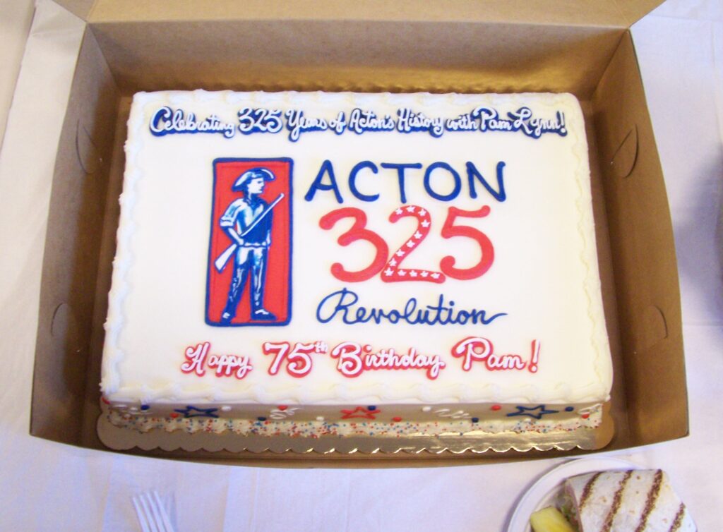 A cake, in red, white, and blue, celebrates both Acton 250 and Pam Lynn's birhday. The cake includes a picture of the Acton minutman logo.