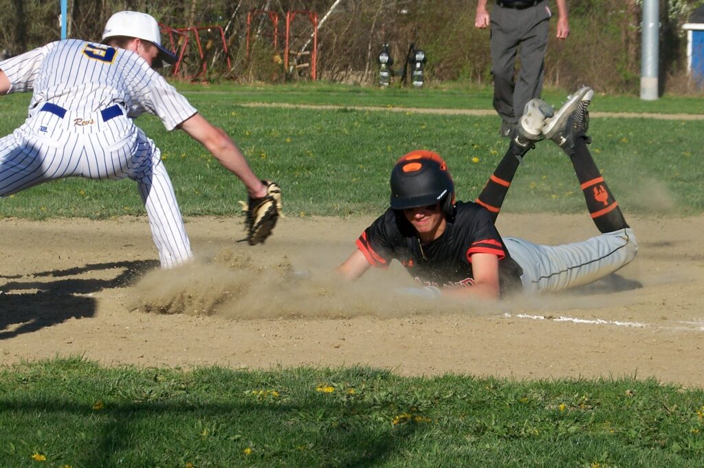 A Wayland player slides into a base on his belly. The Revs player is stretching to tag him before he gets there.