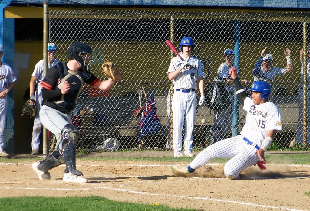 A Revs player slides into a base on his knee, but the Wayland player is ready for him.