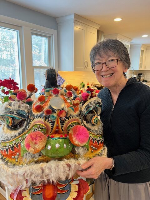 A smiling woman holds the head of a large Chinese dragon puppet.