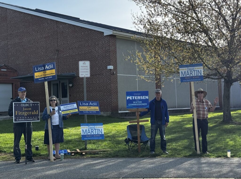 Four people holding campaign signs in front of a brick building.