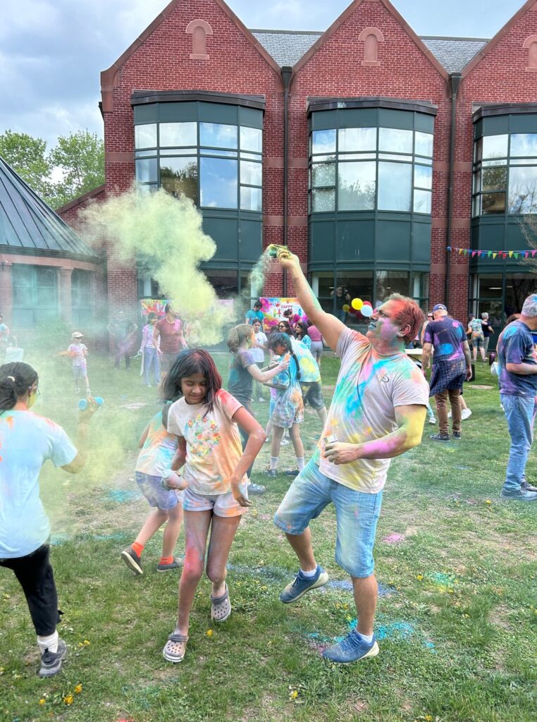 A dye covered kids gets an extra dose of dye from a very colorful man (probably her dad).