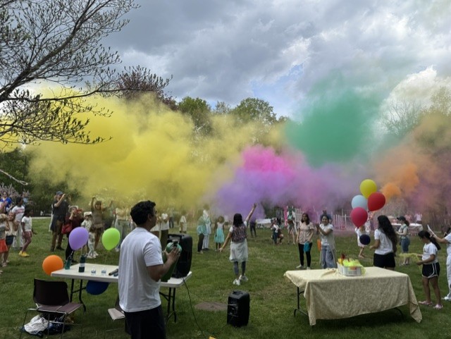 A large crowd of people are underneath colorful clouds of dye in the air -- Yellow, pink, purple, green, and orange (and maybe others).