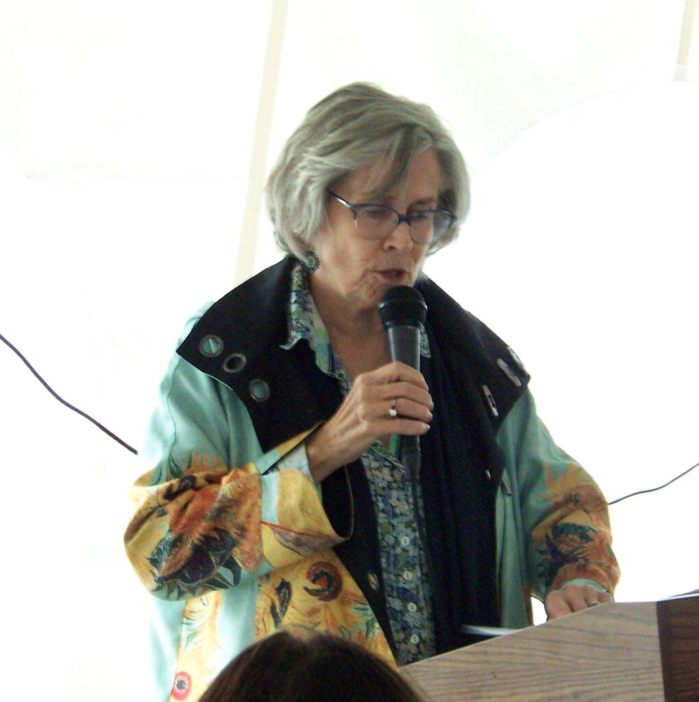 A woman in a flowery green raincoat speaks at a podium.