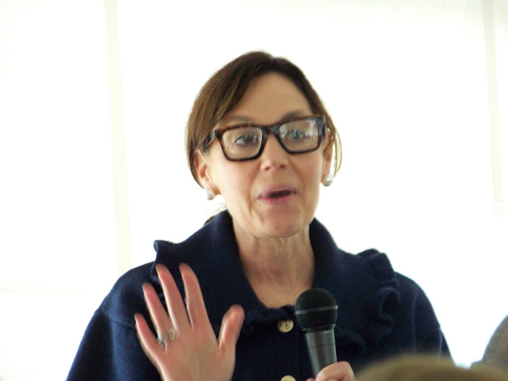 A women with tortoiseshell glasses speaks into a microphone.