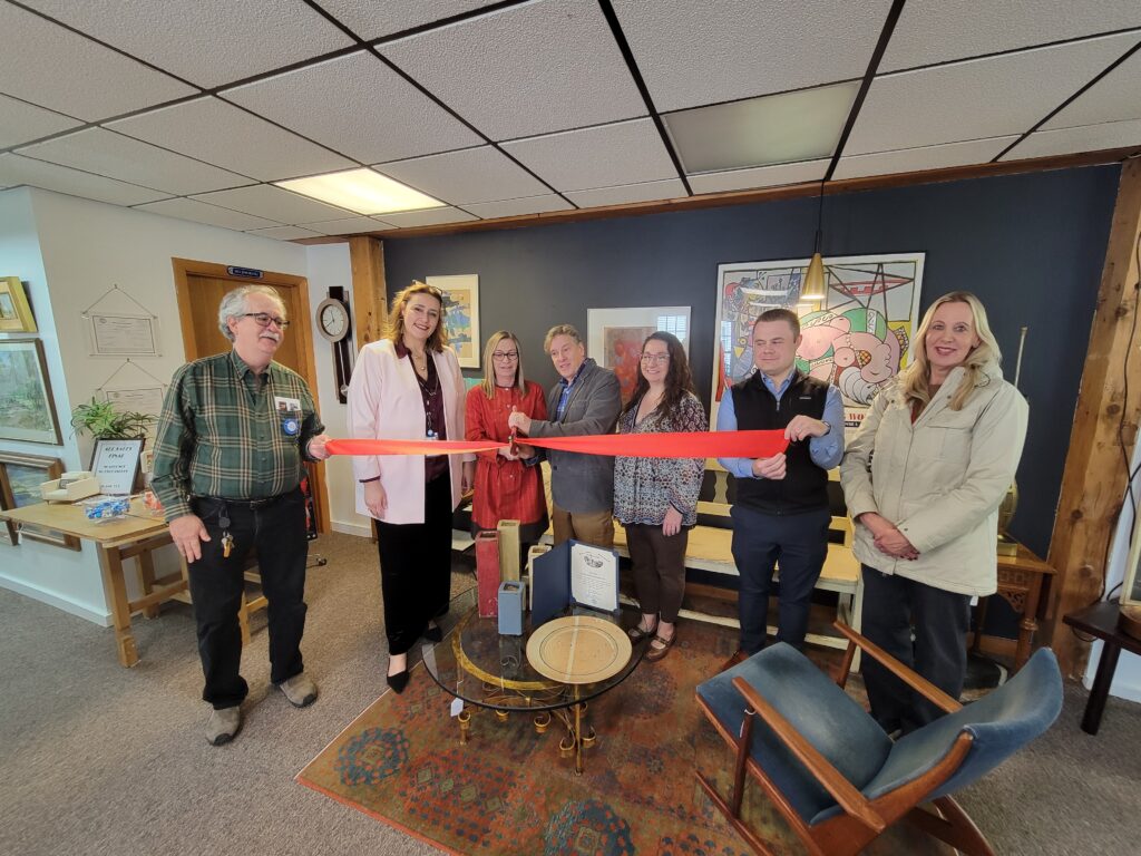 People are lined up with a red ribbon. A man and a woman are holding oversized scissors to cut the ribbon.