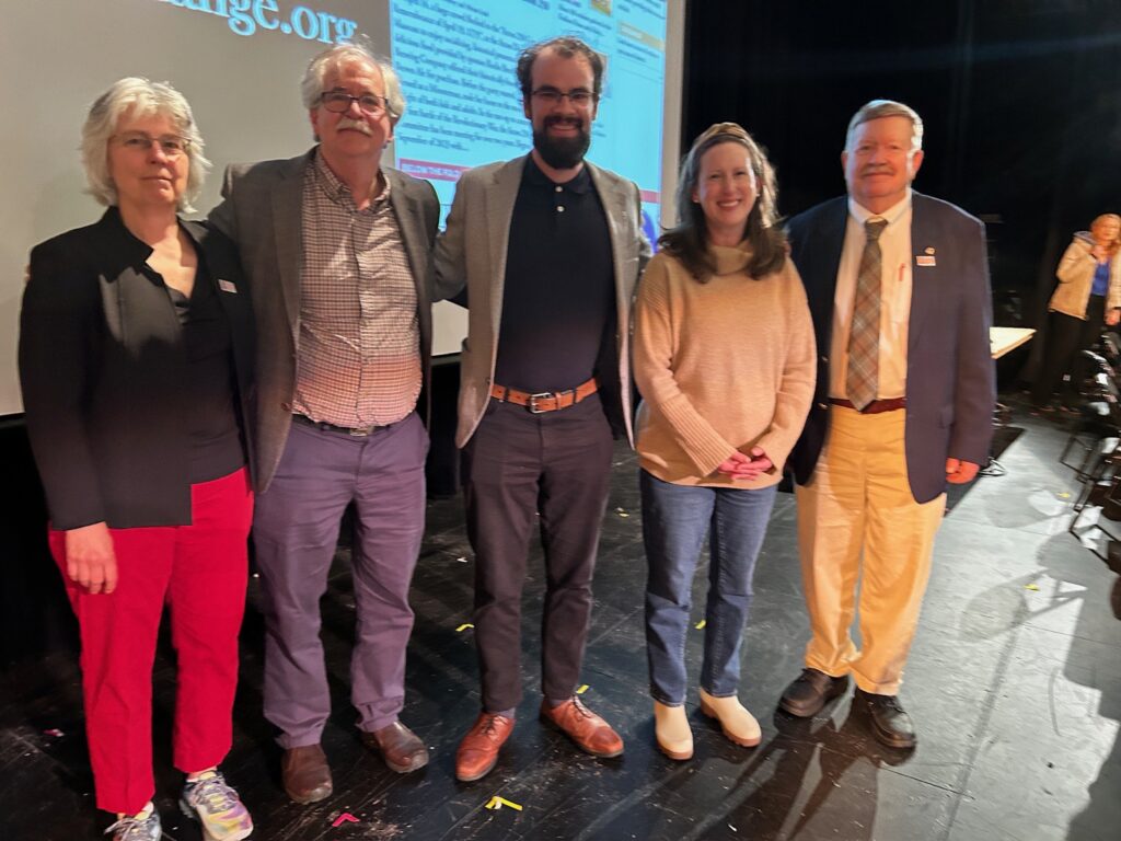 A woman with short hair and bright red pants stands with three men in sport coats and a woman in a brown sweater. They look remarkably awake, given that it's after midnight.