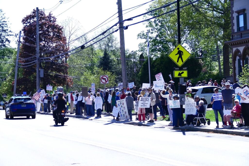 People lined up along the street. Many are carrying signs that say things like "Hands Off!" and "Justice!"