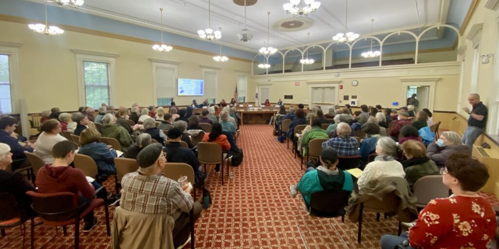 A view from the back of Room 204 in Town Hall. Most of the seats are full of people watching the presenters at the front.