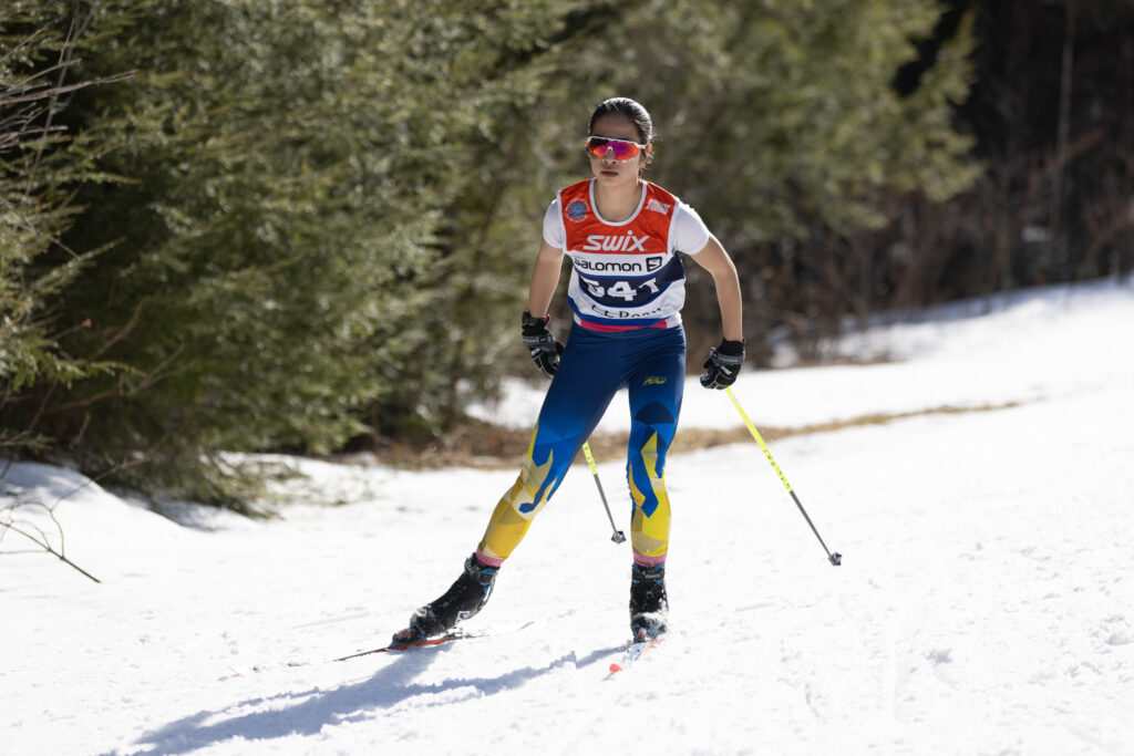 A young woman skiis along a trail; with her arms back and poles behind her. She's wearing a t-shirt and sunglasses -- it's a great day to be out, but the snow is sticky!