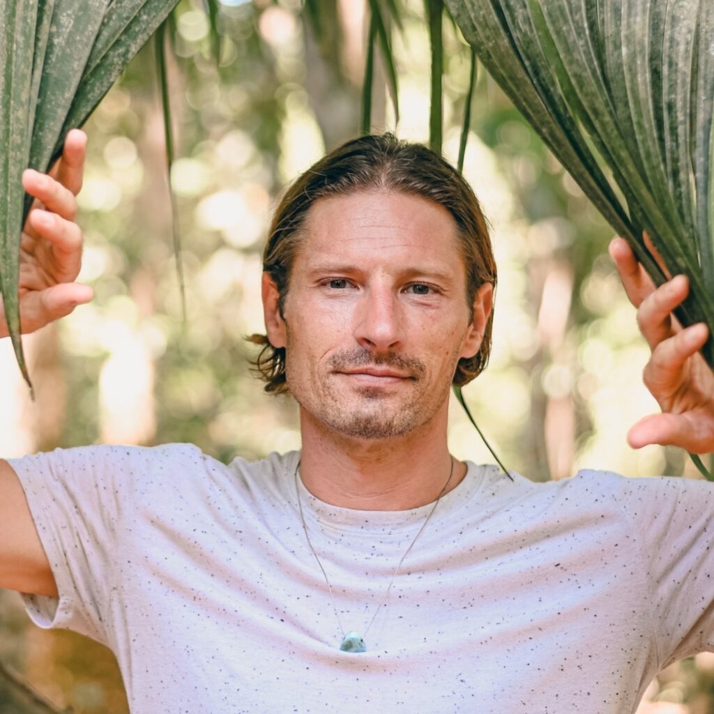 A man wearing a t-shirt and sporting a light beard and mustache looks intently at the camera.