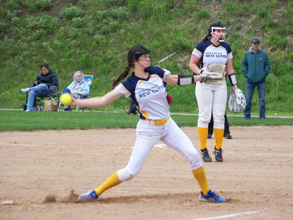 A Revs player with a long brown braid leans back to prepare for a pitch.
