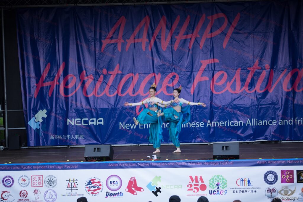 Two women, wearing silky blue costumes, dance in unison.
