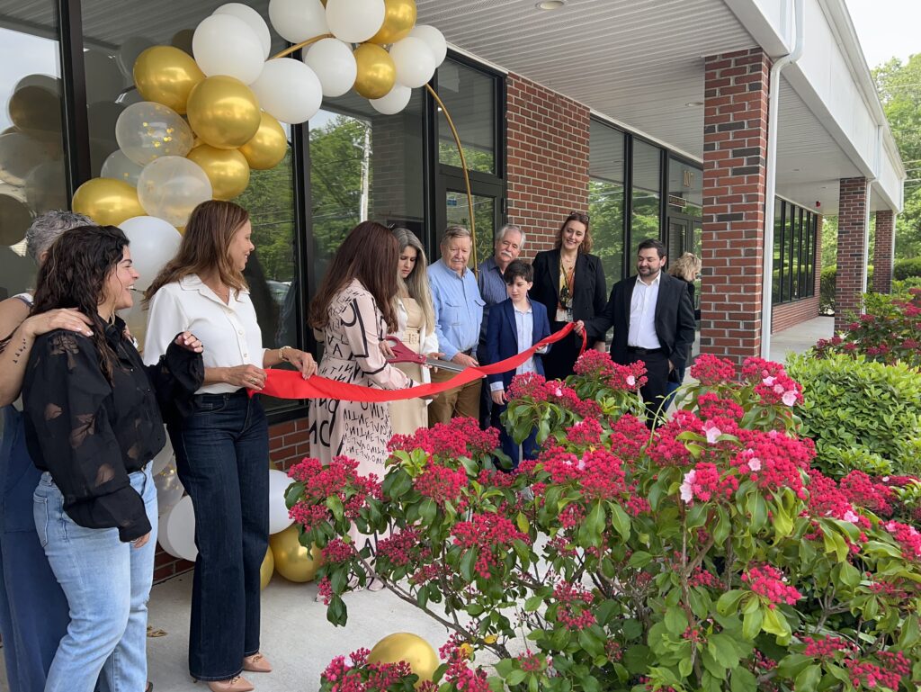 A group of people hold a red ribbon while the new owners wrangle the giant red scissors.