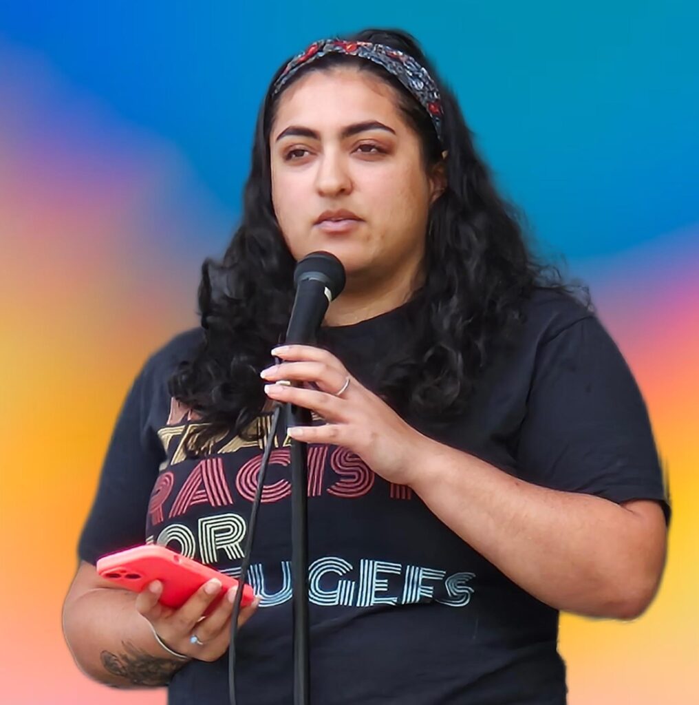 A woman with long black hair speaks into a mic.