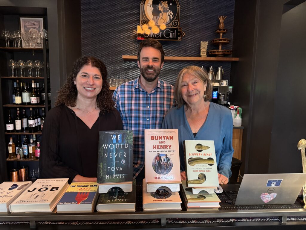Two women and a man stand in front of a book display (all books written by the authors).