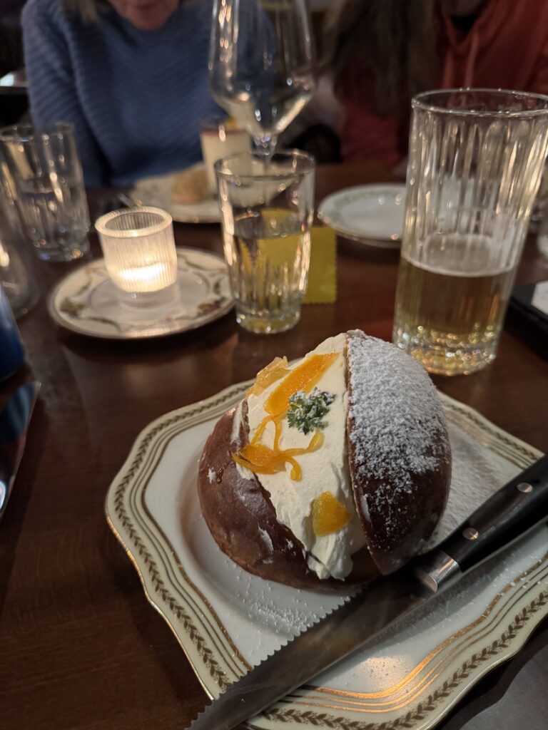 In the foreground, a bun stuffed with ricotta, and covered with powdered sugar. In the background, glasses and a candle.