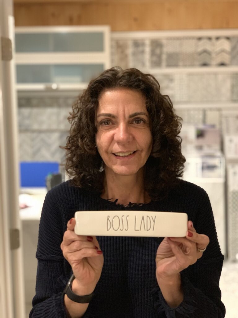 A curly-haired woman holds a tile that says "Boss Lady."