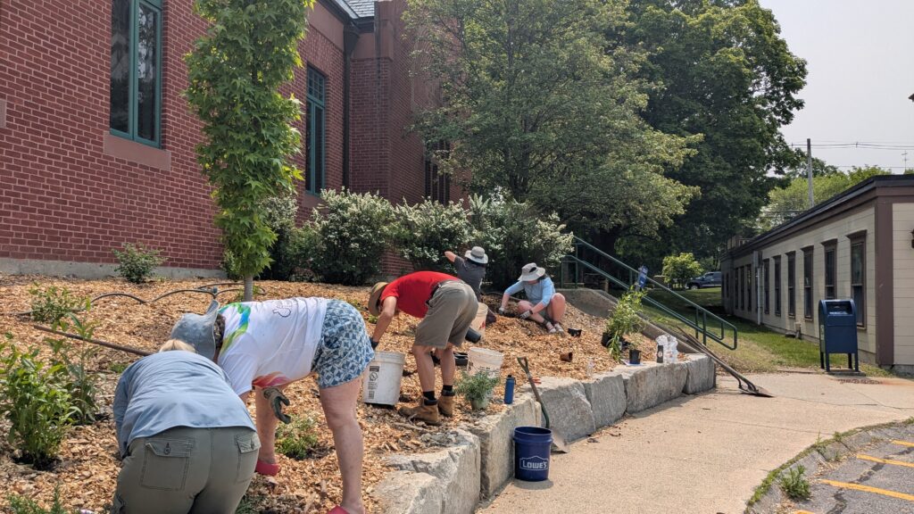 The plastic is gone and at least 5 people are working on the garden. Mostly, you can see gardener's hats and bottoms.