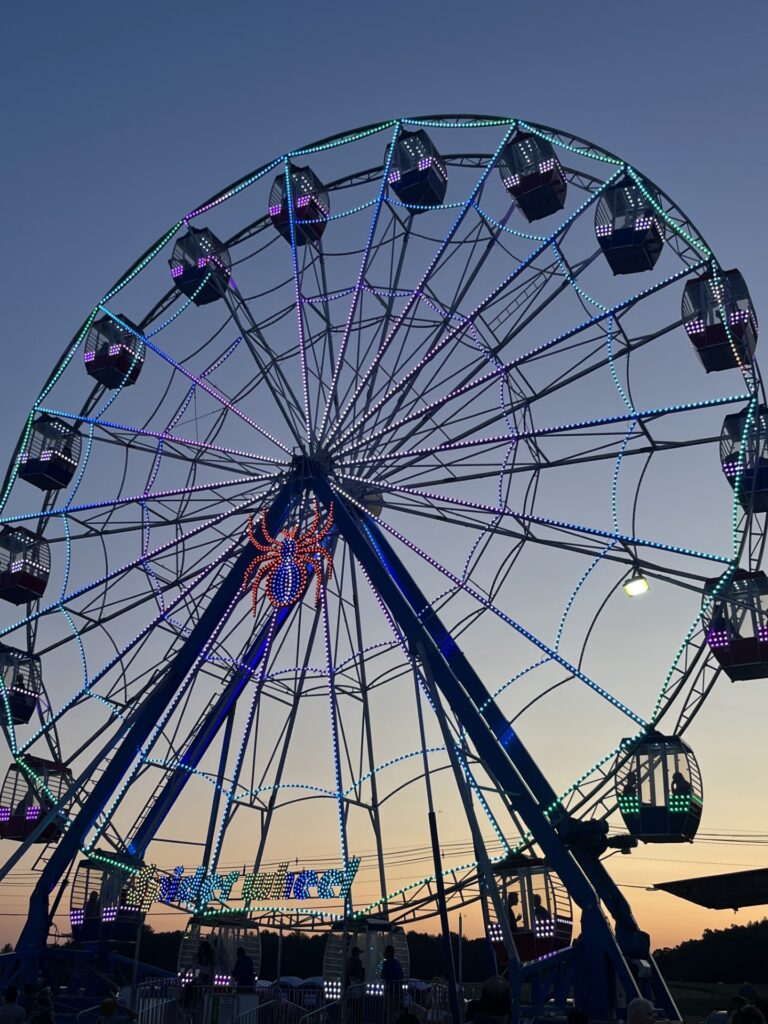 A closed-box ferris wheel reaches into the sky. A pinky-orange sky is in the background.