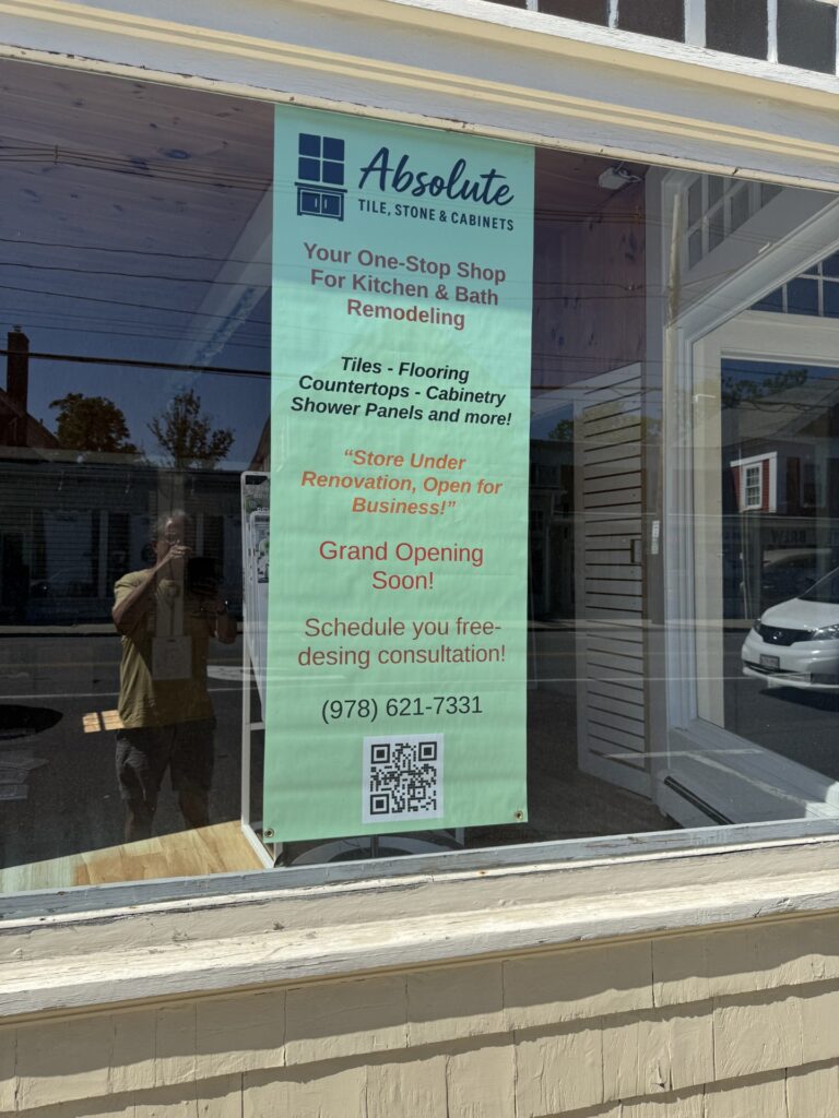 An empty store front with a poster in the window. The poster proclaims that the store is under renovation, but open for business, and Grand Opening Soon!