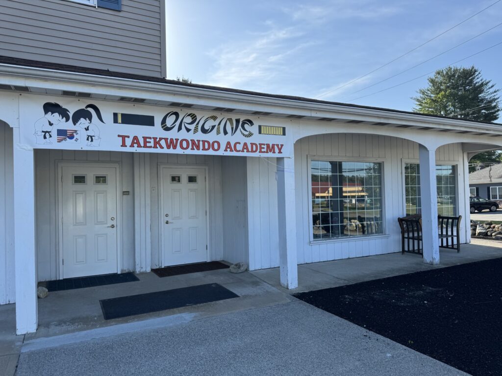 A white building with the sign " Origins Taekwondo Academy" over the door.