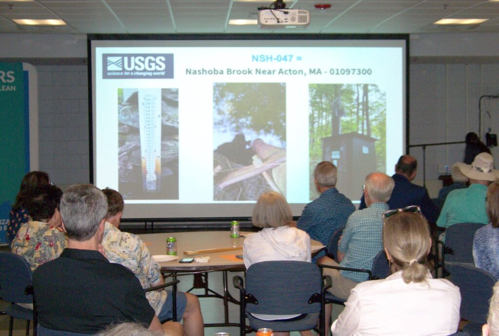 An audience in the foreground, looking at a slide with pictures of the equipment used to measure water quality at Nashoba Brook (location NSH-047)