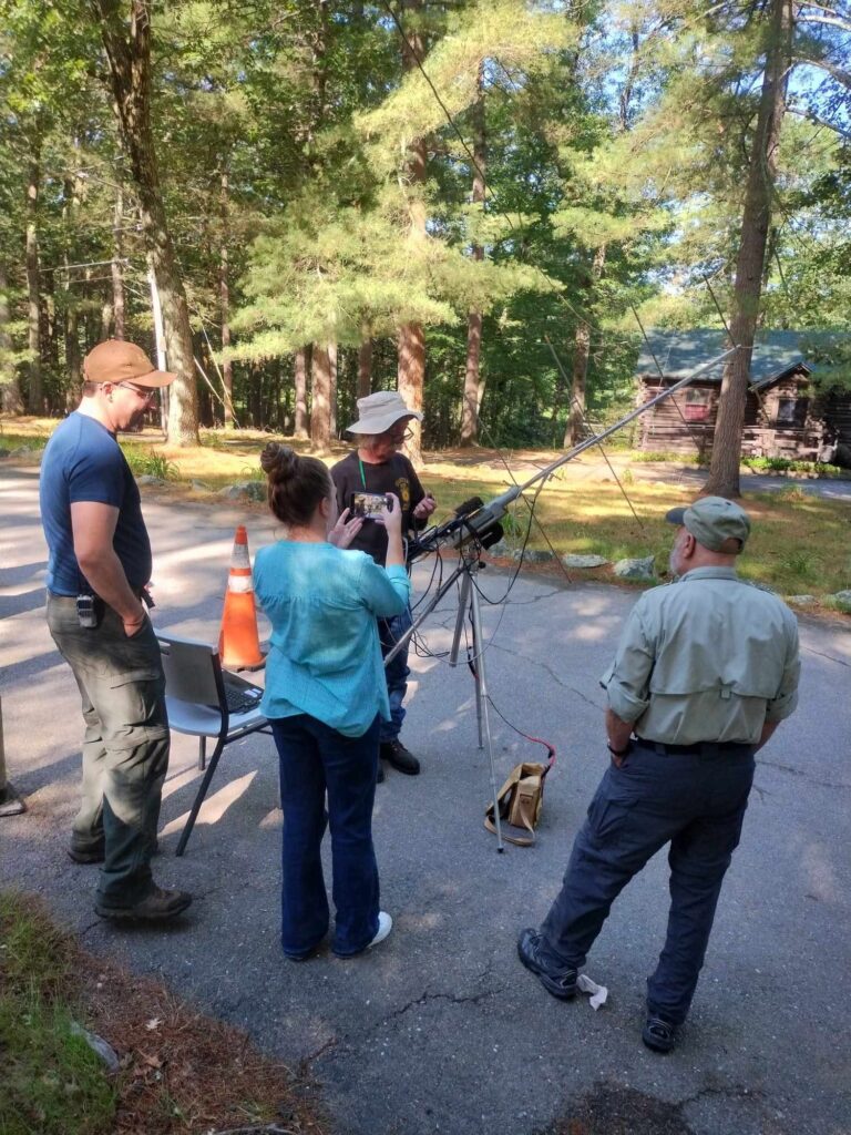 Several people stand around what appears to be a portable antenna in the early morning light.