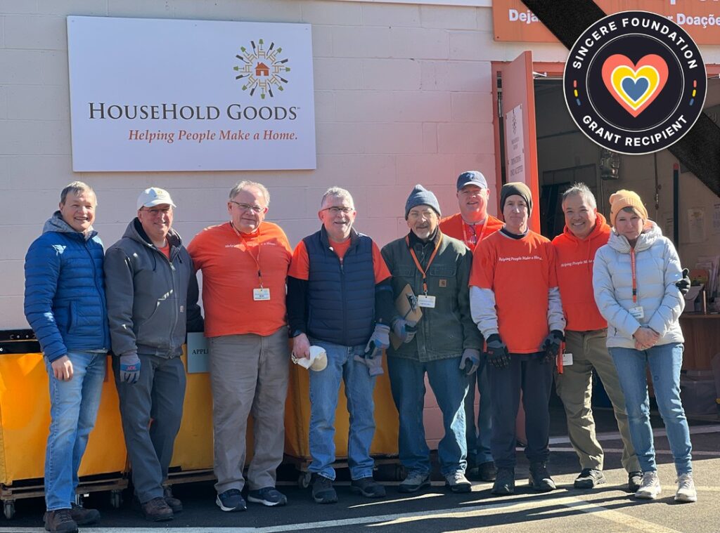 Household Goods workers and volunteers pose in front of the Household Goods sign. The Sincere Foundation Grant Recipient logo is in the top right corner.