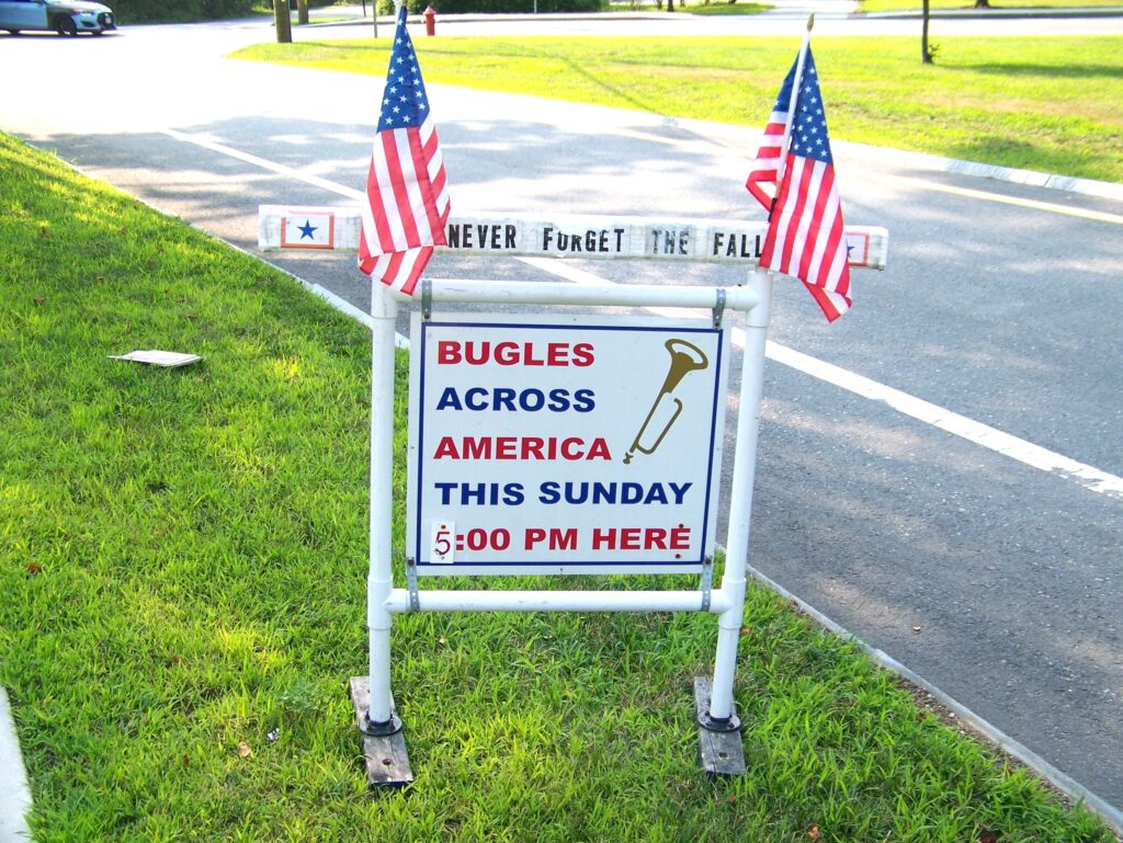 A sign with two American flags that reads:"Bugles Across America this Sunday 5:00 PM here."