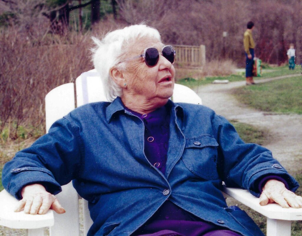 An older woman with short white hair sits in a white Adirondack chair.